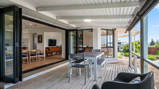 A modern interior with a dining area, kitchen, and a wooden deck with outdoor seating. - Coastal Retreat—Treetop Outlooks by Goolwa Beach (Goolwa South)