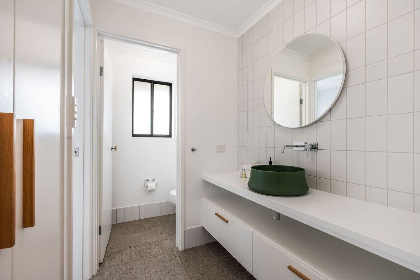 A bathroom with a white tiled wall, a round mirror, a green sink, and a door leading to another room.