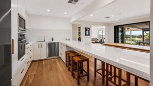 A modern kitchen with white cabinetry, stainless steel appliances, and a wooden bar area. - Coastal Retreat—Treetop Outlooks by Goolwa Beach (Goolwa South)