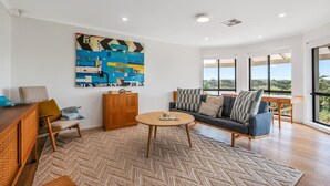 A modern living room with a sofa, coffee table, and a large abstract painting on the wall. - Coastal Retreat—Treetop Outlooks by Goolwa Beach (Goolwa South)