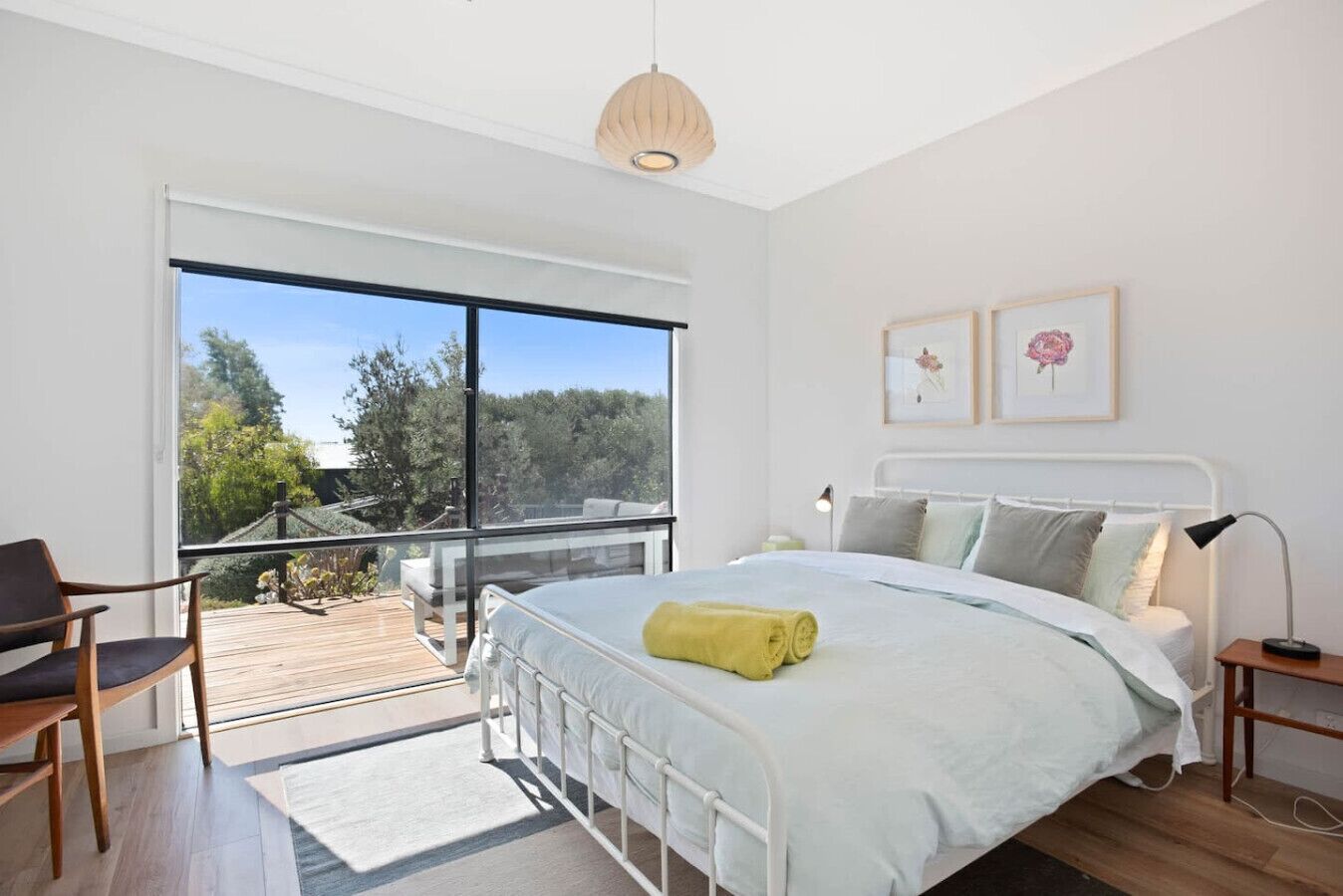 Un dormitorio moderno con un ventanal grande, una cama con una toalla amarilla y dos cuadros en la pared.