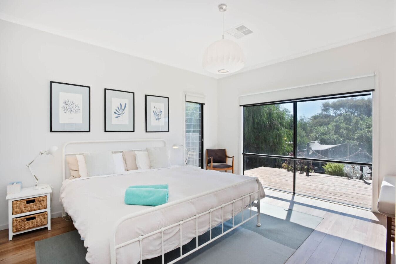 A modern bedroom with a large bed, a nightstand, a chair, and a balcony with a view of greenery.