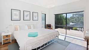 A modern bedroom with a large bed, a nightstand, a chair, and a balcony with a view of greenery.