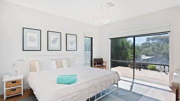 A modern bedroom with a large bed, a nightstand, a chair, and a balcony with a view of greenery.