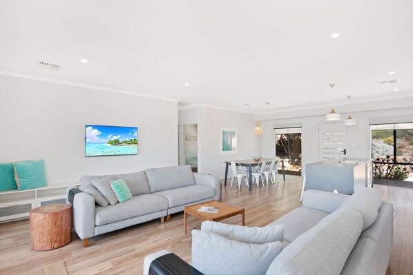 A spacious living room with a grey sofa, a coffee table, and a dining area with white chairs.