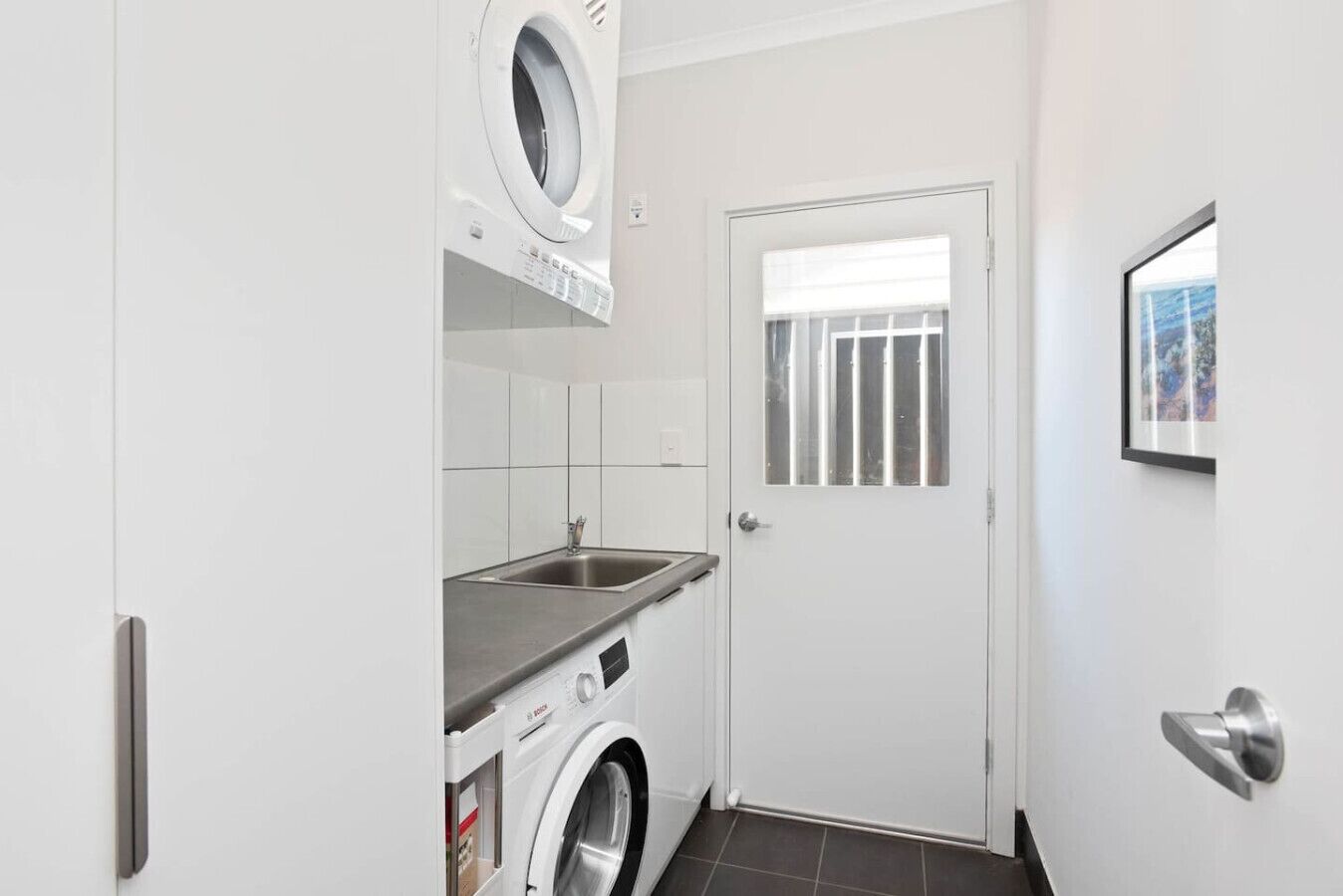 A compact laundry room with a washing machine, a sink, and a door with a window.