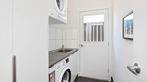 A compact laundry room with a washing machine, a sink, and a door with a window.