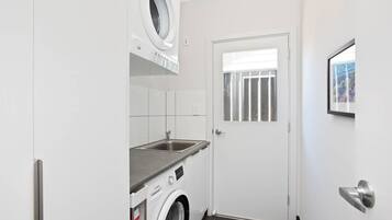 A compact laundry room with a washing machine, a sink, and a door with a window.