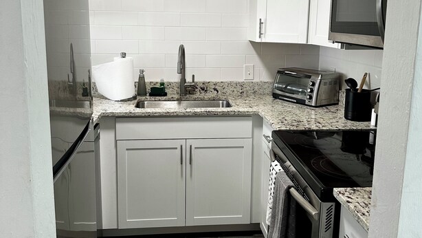 A compact kitchen with white cabinets, a stainless steel sink, a toaster, and a microwave. - Stadium Stay 2 Bedroom (Tallahassee)