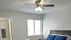 A bedroom with a bed, a ceiling fan, a window, and a door leading to a bathroom. - Stadium Stay 2 Bedroom (Tallahassee)