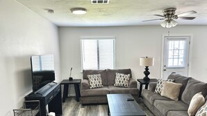 A living room with a sofa, coffee table, TV, and a ceiling fan. - Stadium Stay 2 Bedroom (Tallahassee)
