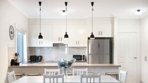 A modern kitchen with white cabinets, a stainless steel refrigerator, and pendant lights. - Brooking’s Perch - Riverside Stay near Cafés & Wharf (Goolwa)