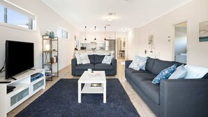 A modern living room with a flat-screen TV, two dark sofas, a white coffee table, and a dark rug. - Brooking’s Perch - Riverside Stay near Cafés & Wharf (Goolwa)