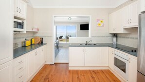 Een moderne keuken met witte kasten, een inbouwoven en een groot raam met uitzicht op de omgeving.