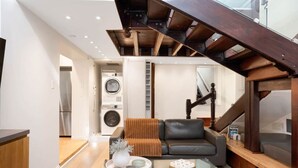 A modern living room with a glass coffee table, a leather sofa, and a staircase with exposed wooden beams. - The Gordon Hideaway, Heart of Glenelg, Luxury (Glenelg)