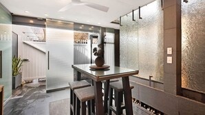 A modern kitchen with a glass-top table, bar stools, and a ceiling fan. - The Gordon Hideaway, Heart of Glenelg, Luxury (Glenelg)