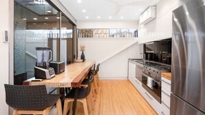 A modern kitchen with a wooden dining table, a blender, a kettle, and stainless steel appliances. - The Gordon Hideaway, Heart of Glenelg, Luxury (Glenelg)
