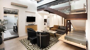 A modern living room with a sofa, chairs, a coffee table, and a TV. There is a staircase with a glass railing leading to an upper level. - The Gordon Hideaway, Heart of Glenelg, Luxury (Glenelg)