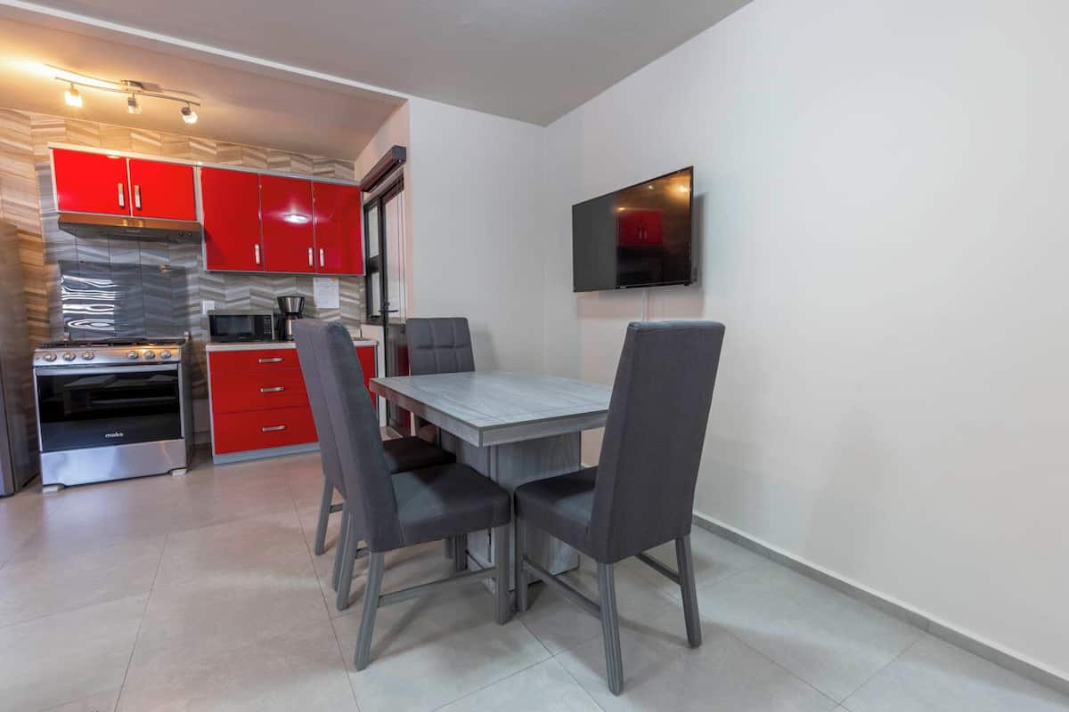 A compact kitchen with red cabinets, a built-in microwave, a stove, and a dining table with four chairs.