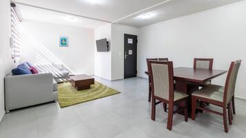 A modern living room with a sofa, a dining table with chairs, a staircase, and a door with a sign.