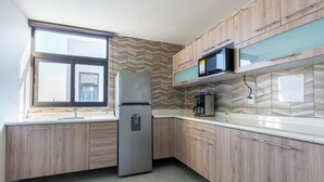A modern kitchen with wooden cabinetry, a stainless steel refrigerator, a microwave, and a coffee maker. - Lofts by Verticca San Francisco (Tecámac)