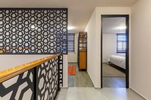 A narrow hallway with a geometric-patterned wall, a wooden railing, and a bed in the adjacent room. - Lofts by Verticca San Francisco (Tecámac)
