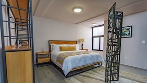 A bedroom with a bed, bedside tables, a lamp, a window, and a decorative metal partition. - Lofts by Verticca San Francisco (Tecámac)
