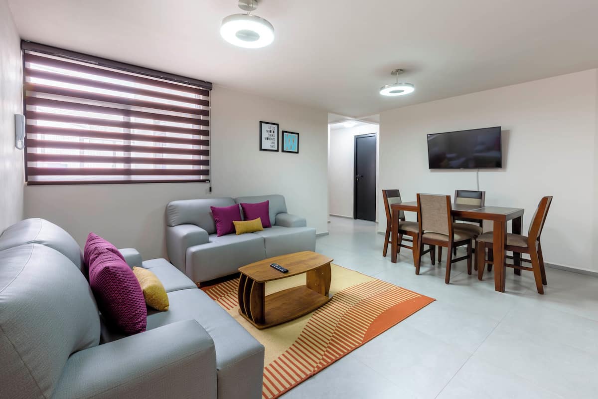 A modern living room with a grey sofa, a wooden coffee table, and a dining area with wooden chairs and a table.