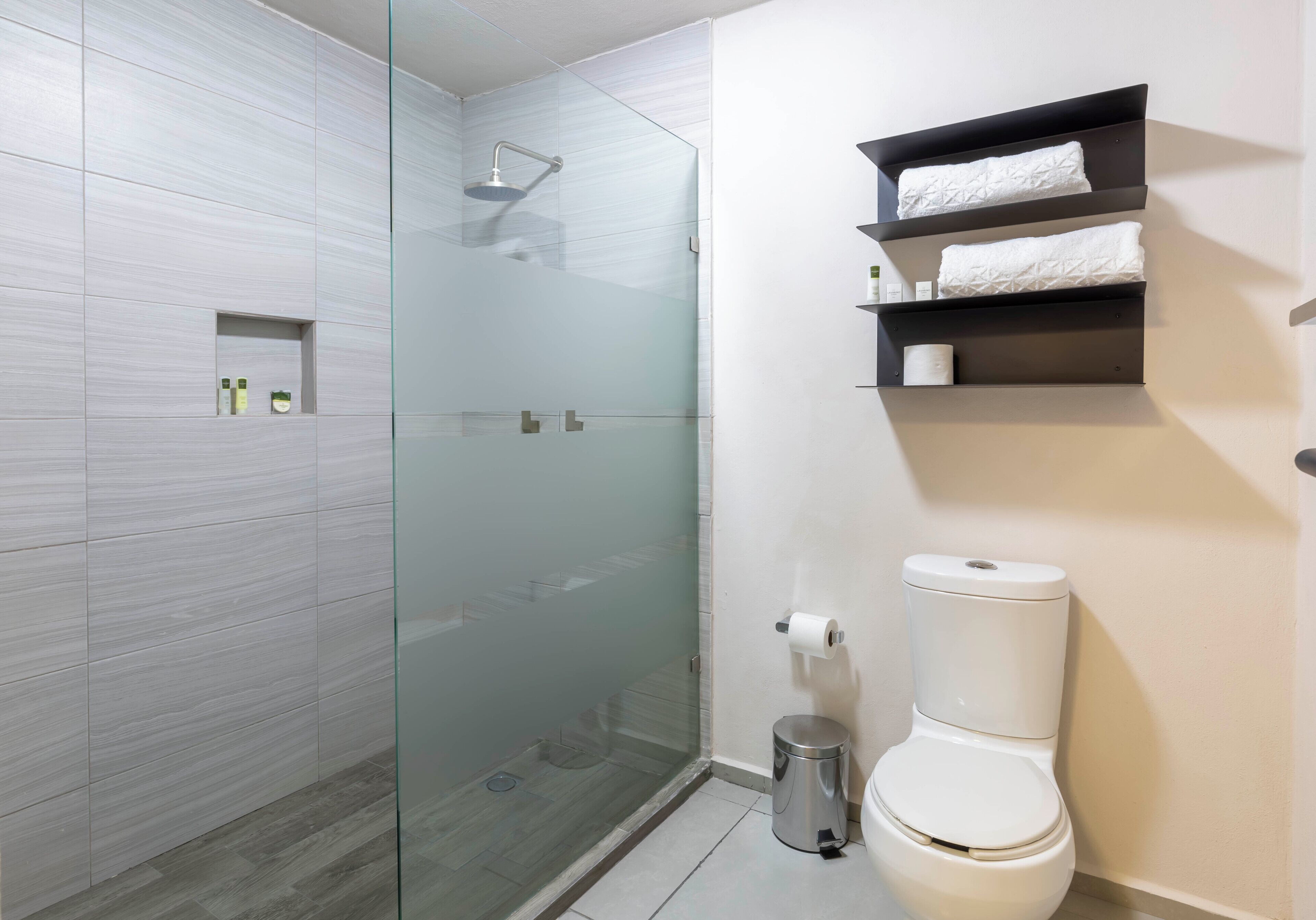 A modern bathroom with a glass shower enclosure, a toilet, and built-in shelves with toiletries.