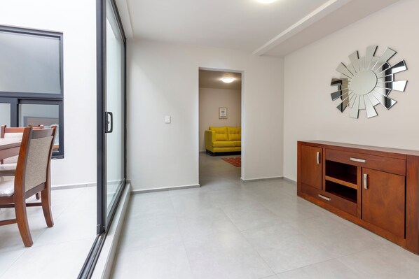 A hallway with a wooden cabinet, a yellow sofa, and a large mirror on the wall. - Lofts by Verticca San Francisco (Tecámac)