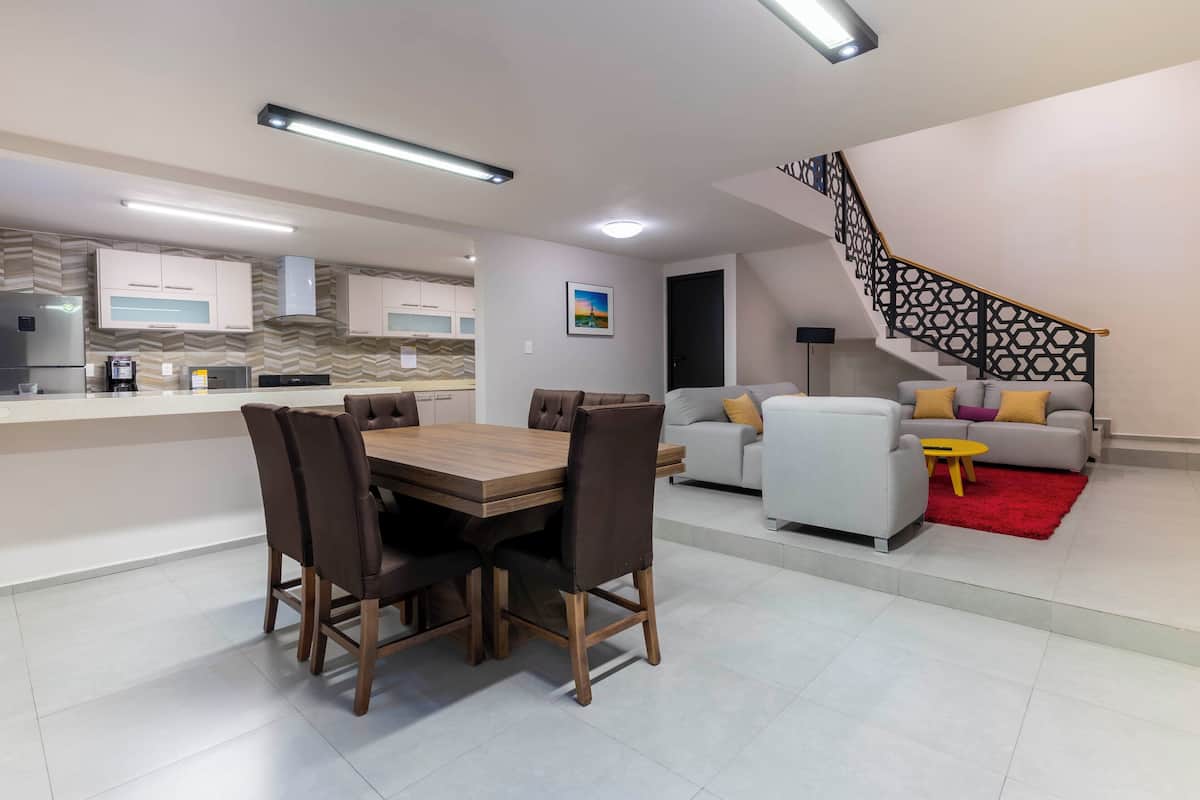 A modern living space with a dining area, kitchen, staircase, and a sofa set.
