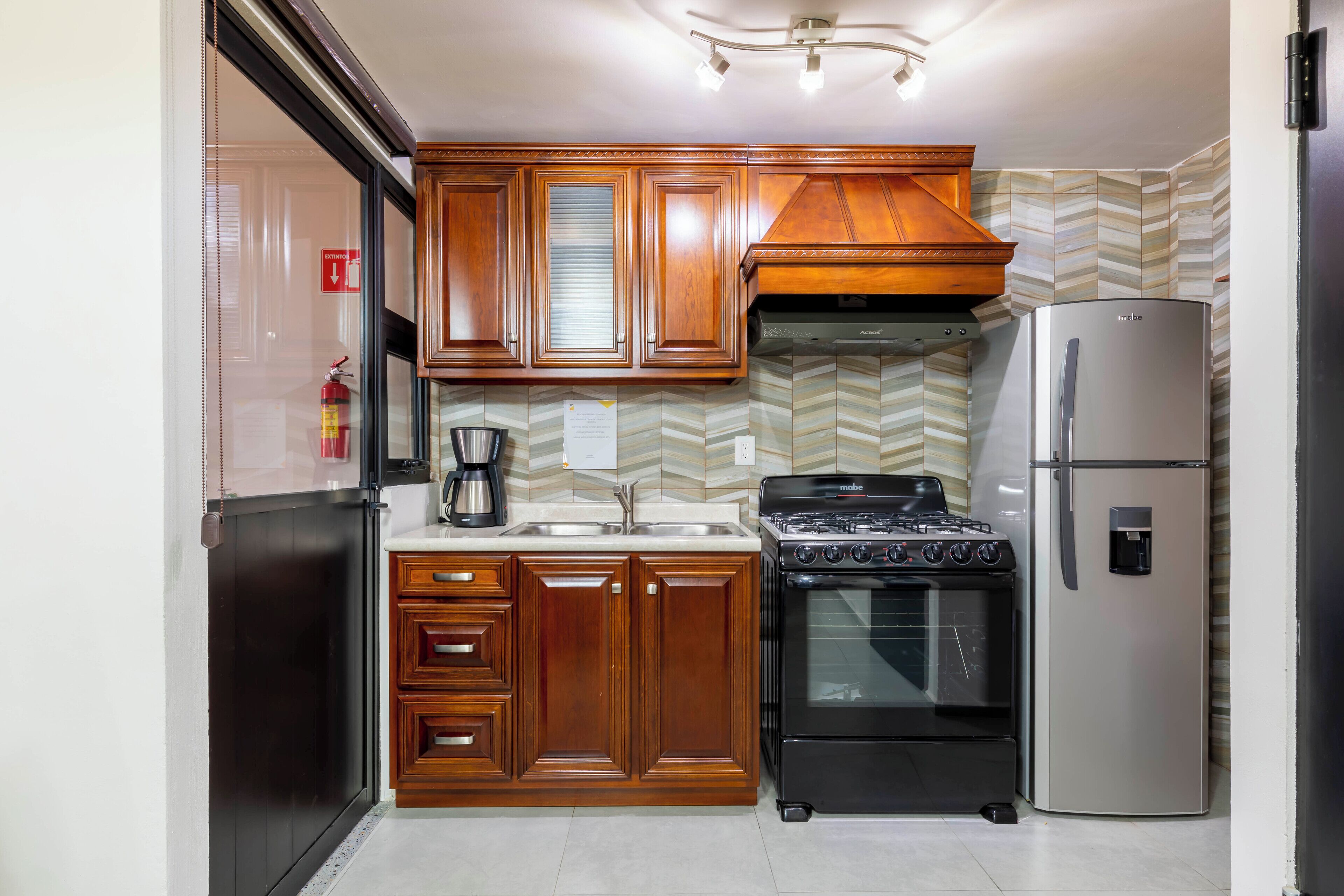 Una cocina con armarios de madera, un refrigerador de acero inoxidable, una estufa y una cafetera.