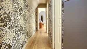Un couloir avec un papier peint à motifs, un plancher en bois et un luminaire au plafond.
