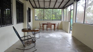 A room with a dining table and chairs, a rocking chair, and large windows with a view of trees. - Charming 2-bedroom house with WiFi, AC in Pavones (Pavones)