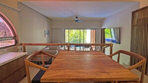 A modern dining area with a wooden table and benches, a ceiling fan, and a view of the outdoors through large windows. - Luxury beachfront condo with private pool & fast internet (Bahías de Huatulco)