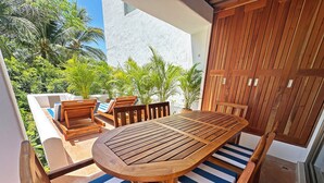 A wooden table with striped cushions, surrounded by wooden chairs, set on a patio with a view of greenery and a building in the background. - Luxury beachfront condo with private pool & fast internet (Bahías de Huatulco)