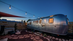 A silver RV parked in a backyard with a stone pathway, wooden fence, and string lights.