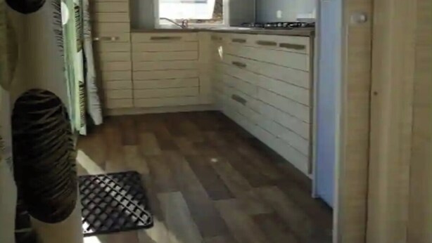 A compact kitchen with wooden cabinets, a window, and a built-in stove. - Mobile home 32m2 at the farm (Souvigny-en-Sologne)