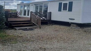 A mobile home with a deck, outdoor seating, and a gravel driveway. - Mobile home 32m2 at the farm (Souvigny-en-Sologne)
