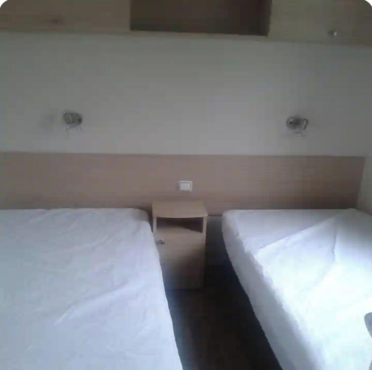 A hotel room with two single beds, a small bedside table, and a wall-mounted light fixture.