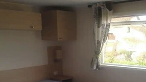 A small, single-bed room with a window, a wooden wardrobe, and a curtain. - Mobile home 32m2 at the farm (Souvigny-en-Sologne)