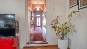 A hallway with a red chair, a white potted plant, and a TV on the left. - Bylund Cottage – Historic Charm in the Heart of Albany (MIRA MAR)