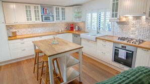 A modern kitchen with white cabinets, a wooden countertop, a built-in microwave, a coffee machine, and a gas stove. - Bylund Cottage – Historic Charm in the Heart of Albany (MIRA MAR)
