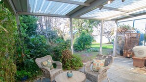 An outdoor patio with wicker furniture, a round table, and a covered area with a metal roof. - Bylund Cottage – Historic Charm in the Heart of Albany (MIRA MAR)