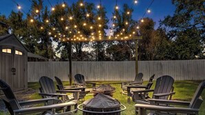 An outdoor seating area with Adirondack chairs and a fire pit, under a pergola with string lights. - Charming 2-bedroom Home Lakeland (Lakeland)