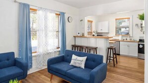 A compact living space with a kitchenette, a blue sofa with a 'welcome home' pillow, and a wooden floor. - Charming 2-bedroom Home Lakeland (Lakeland)