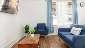 A living room with a blue sofa, a wooden coffee table, a blue armchair, and a potted plant. - Charming 2-bedroom Home Lakeland (Lakeland)