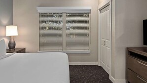 Une chambre d’hôtel avec un lit, une lampe de chevet, un téléviseur et une fenêtre avec des stores.