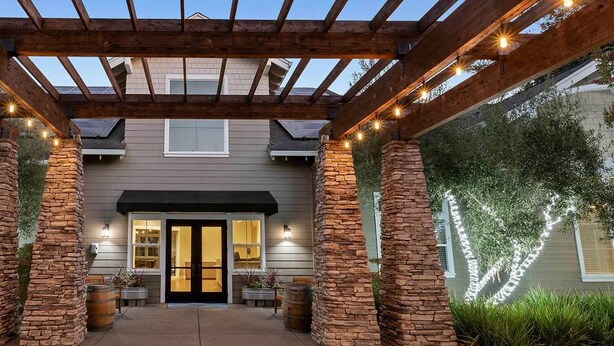 Une terrasse couverte avec des piliers en pierre, une pergola en bois et des guirlandes lumineuses.