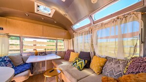 A cozy RV interior with a dining area, seating with cushions, and large windows. - Airstream w/ Private Hot Tub (Unit K) - 4 Person Airstream with Private Hot Tub (Williams)